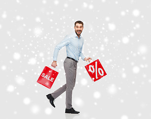 Image showing smiling man with red shopping bags over snow