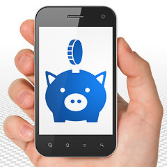 Image showing Banking concept: Hand Holding Smartphone with Money Box With Coin on display