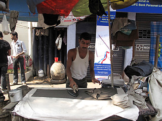 Image showing Streets of Kolkata. Man presses clothes using a traditional charcoal heated iron