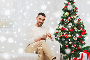 Image showing smiling man with smartphone at home for christmas