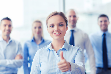 Image showing smiling businesswoman showing thumbs up in office