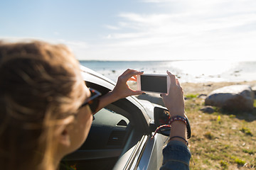 Image showing happy young woman in car with smartphone at sea