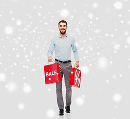 Image showing smiling man with red shopping bags over snow