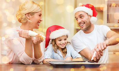 Image showing happy family in santa helper hats making cookies