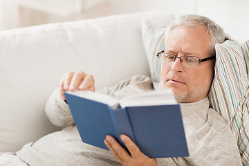 Image showing senior man lying on sofa and reading book at home