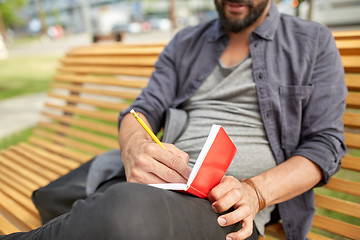 Image showing close up of man writing to notebook on city street