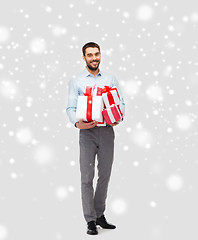 Image showing happy young man holding christmas gifts over snow