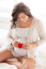 Image showing happy pregnant woman with red heart in bed at home