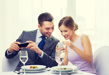 Image showing smiling couple with appetizers and smartphones