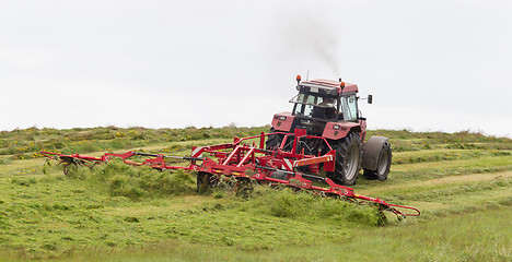 Image showing Farmer uses tractor to spread hay on the field