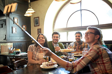 Image showing happy friends with selfie stick at bar or pub