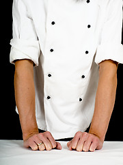 Image showing Professional chef leaning firmly onto a table with white cover