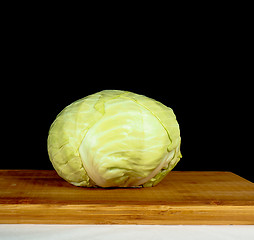 Image showing Whole cabbage isolated towards black, on a wooden cutting board