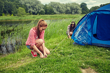 Image showing smiling friends setting up tent outdoors