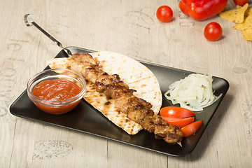 Image showing shashlik. kebab skewer, black rectangular plate. sauce and onions