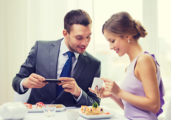 Image showing smiling couple with sushi and smartphones
