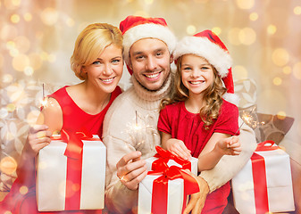 Image showing smiling family holding gift boxes and sparkles