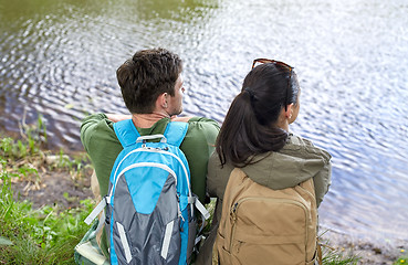 Image showing couple with backpacks sitting on river bank