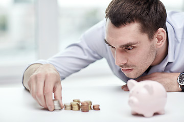 Image showing businessman with piggy bank and coins at office