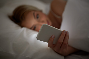 Image showing young woman with smartphone in bed at home bedroom