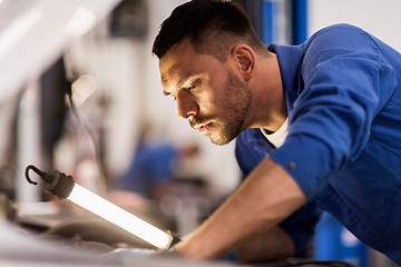 Image showing mechanic man with lamp repairing car at workshop