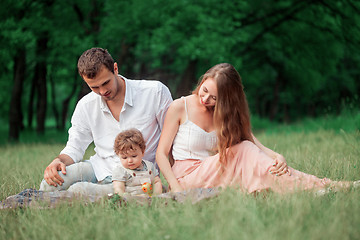 Image showing Young beautiful father, mother and little toddler son against green trees