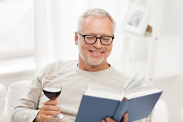 Image showing happy senior man drinking wine and reading book