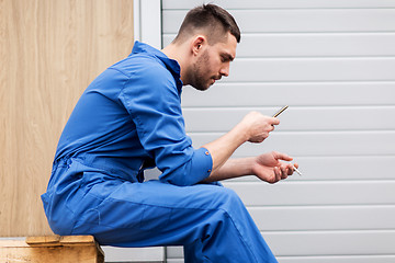 Image showing auto mechanic smoking cigarette at car workshop