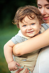 Image showing Young beautiful mother hugging her little toddler son against green grass. Happy woman with her baby boy on a summer sunny day. Family walking on the meadow.