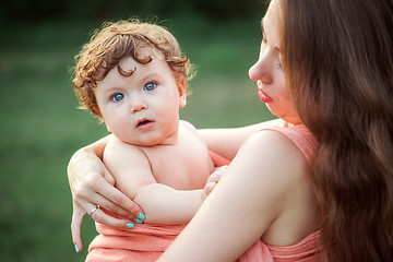 Image showing Young beautiful mother hugging her little toddler son against green grass. Happy woman with her baby boy on a summer sunny day. Family walking on the meadow.