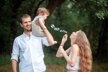 Image showing Young beautiful father, mother and little toddler son against green trees