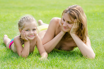 Image showing Young mother lying on green grass and looking at his five-year daughter who is lying near