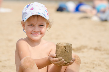 Image showing Girl keeps hands on the turret of sand sitting on a river beach