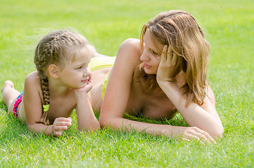 Image showing Young mother and five year old daughter lying on green grass and looking at each other