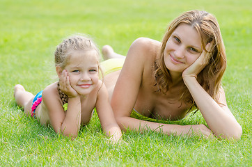 Image showing Young mother and five year old daughter lying on green grass and looking to the frame
