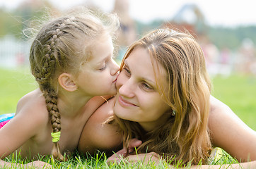 Image showing The five-year daughter kissing her mother lying on green grass lawn
