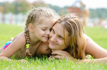 Image showing Five-year cute daughter pressed her face to the mother\'s face on a green grass lawn