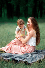 Image showing Young beautiful mother sitting with her little son against green grass. Happy woman with her baby boy on a summer sunny day. Family walking on the meadow.