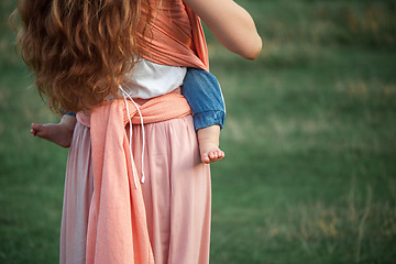 Image showing Young beautiful mother hugging her little toddler son against green grass. Happy woman with her baby boy on a summer sunny day. Family walking on the meadow.