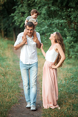 Image showing Young beautiful father, mother and little toddler son against green trees