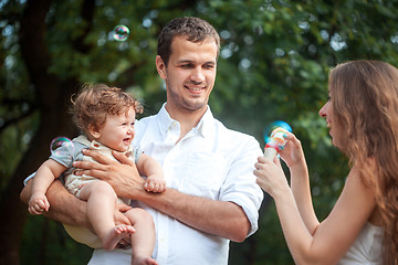 Image showing Young beautiful father, mother and little toddler son against green trees