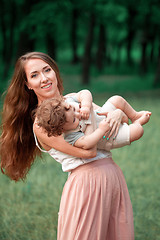 Image showing Young beautiful mother hugging her little toddler son against green grass. Happy woman with her baby boy on a summer sunny day. Family walking on the meadow.