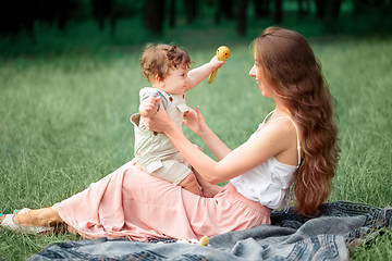 Image showing Young beautiful mother sitting with her little son against green grass. Happy woman with her baby boy on a summer sunny day. Family walking on the meadow.