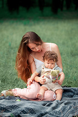 Image showing Young beautiful mother sitting with her little son against green grass. Happy woman with her baby boy on a summer sunny day. Family walking on the meadow.