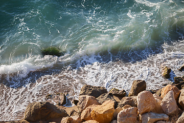 Image showing Beautiful large yellow stones in green waves on sea coast