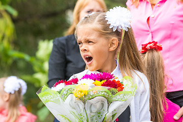 Image showing First grader with a bouquet of flowers yawns at school in a crowd