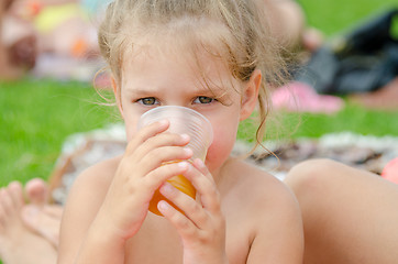 Image showing The girl drinks juice from a plastic disposable cup on a picnic