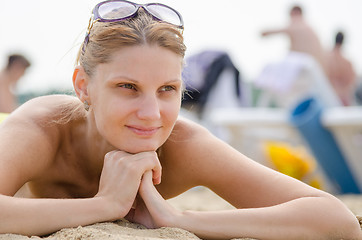 Image showing Young girl lying on the sandy beach against the backdrop of other travelers and smiling looks into the distance