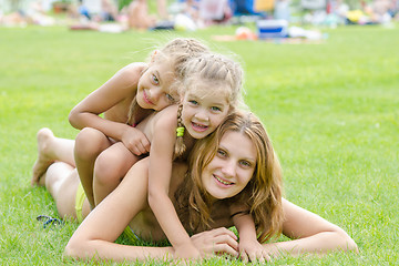 Image showing Two daughters happily sit on mom back, hot summer day relaxing on the green lawn