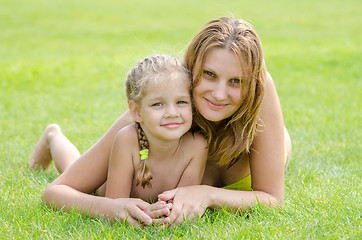 Image showing Young mother and five year old daughter hugging lying on green grass and looking to the frame